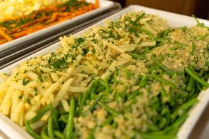 Ein Buffet-Behälter, gefüllt mit grünen Bohnen mit Zwiebeln und gelben Kartoffelstiften mit Kräutern.