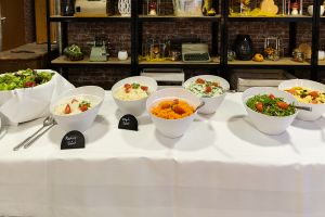 Weiß eingedecktes Salatbuffet mit diversen Salatschüsseln und kleinen Beschriftungstafeln wie „Rettich-Salat“.