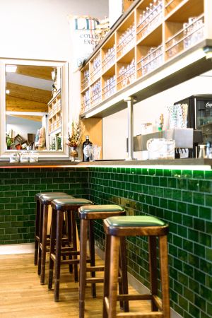 Bar-Bereich mit Holzstühlen, dunkelgrün gefliester Theke und einem Wandspiegel.