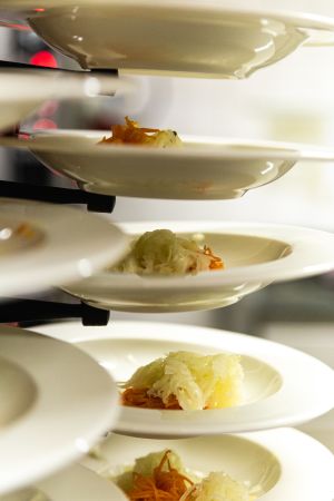 Mehrere weiße, tiefe Teller sind in einem Regal gestapelt, jeweils mit einer kleinen Portion Krautsalat vorbereitet.