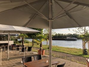 Blick von einer schattigen Terrasse mit Holztisch auf ein vorbeifahrendes Frachtschiff.