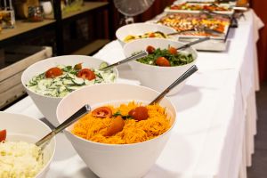 Weiße Schüsseln an einem Buffet, gefüllt mit Karottensalat, Gurkensalat und grünem Salat mit Tomatengarnitur.