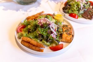 Ein weißer Teller mit gemischtem Salat, gebratenem Lachs, panierten Garnelen und einem Dressing.
