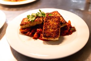 Drei panierte, goldbraun gebratene Tofustücke auf einem Bett aus rotem Gemüse auf einem weißen Teller.