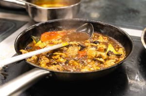 Eine dampfende Pfanne auf einem Herd, gefüllt mit Geschnetzeltem in dunkler Soße, Pilzen und Gemüse.