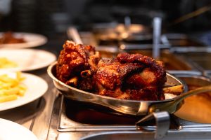 Zwei knusprige Schweinshaxen in einer Metallpfanne in einem Warmhaltebehälter einer Restaurantküche.