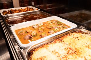 Warmhaltebuffet mit überbackenem Auflauf, Fleischmedaillons in Schnittlauchsauce, Braten und Grillfleisch in Edelstahlbehältern.