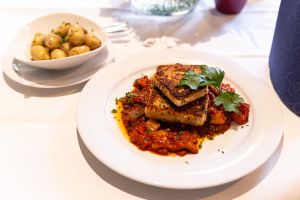 Ein weißer Teller mit gebratenem Tofu auf einem Paprika-Gemüsebett, daneben eine Schale mit kleinen Kartoffeln.
