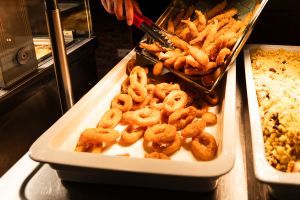 Eine Servierschale am Buffet mit frittierten Calamari-Ringen, in die mit einer Zange panierte Garnelen gefüllt werden.