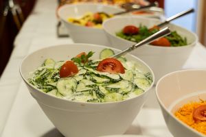 Weiße Servierschüssel mit frischem Gurkensalat in Joghurt-Dill-Dressing, garniert mit Tomatenspalten.