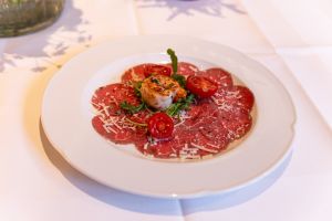 Ein weißer Teller mit Rindercarpaccio, garniert mit einer Garnele, Kirschtomaten, Rucola und Parmesan.