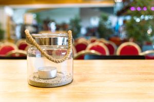Glasschale mit Sand, Teelicht und Kordelhenkel auf einem hellen Holztisch.