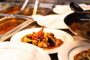 Eine Kelle schöpft dampfendes Geschnetzeltes mit Gemüse aus einer Pfanne auf einen weißen Teller.