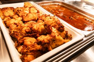 Ein Warmhaltebehälter am Buffet mit gebratenen Hähnchenteilen neben einer Schale mit dunkler Sauce.