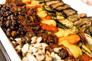 Eine Schale mit mediterranen Antipasti aus schwarzen Oliven, getrockneten Tomaten, gegrillten Zucchini, Paprikastreifen und Champignons.