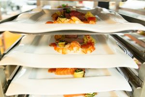 Mehrere weiße Teller mit Vorspeisen, gestapelt in einem Transportregal, bereit zum Servieren.