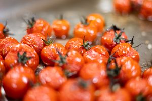 Nahaufnahme von geschmorten Kirschtomaten mit grünem Stielansatz auf einem Blech.