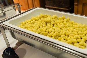 Edelstahl-Chafing-Dish gefüllt mit goldgelben Gnocchi, davor ein kleines Schild mit der Aufschrift „Gnocchi“.